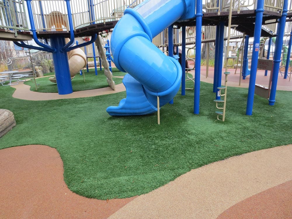 Playground with a blue tunnel slide, pink slides, and toys on artificial grass