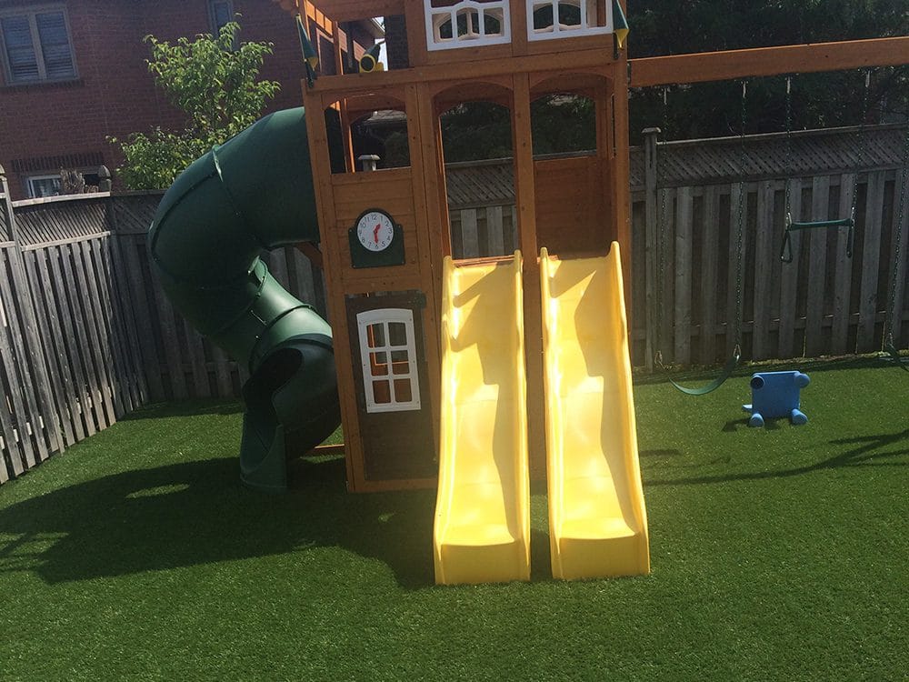 Backyard play structure with yellow slides and a spiral tube slide on artificial grass