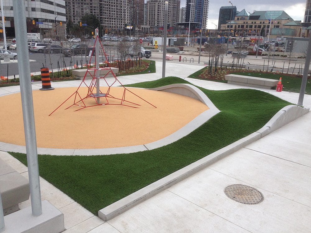 Urban playground with a red rope‑climbing structure and sculpted artificial turf mounds