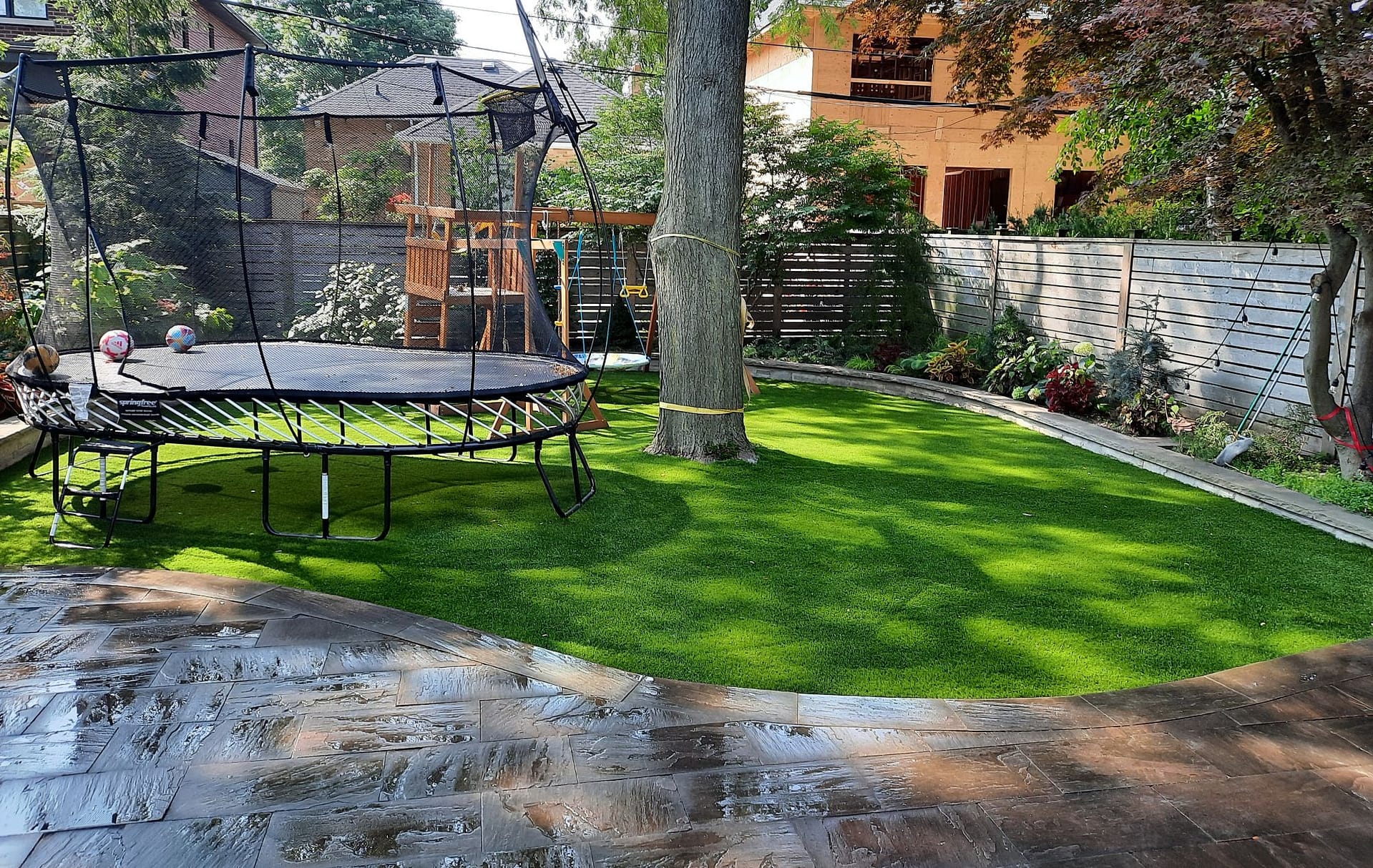 Backyard trampoline with safety net on Optimum Play artificial grass surrounded by trees