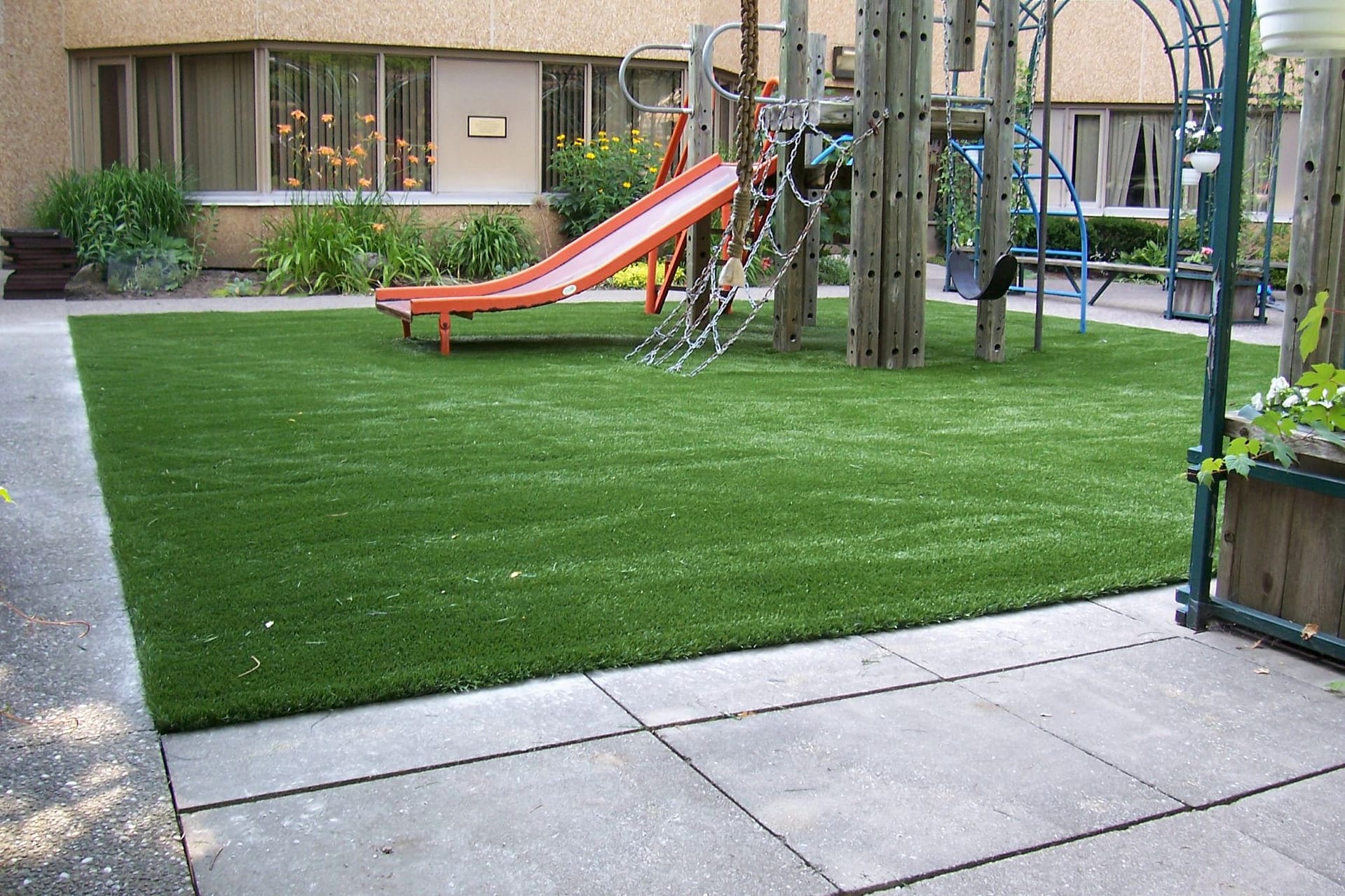 Toronto daycare playground with slides and climbing structures on Optimum Play artificial grass surrounded by trees and a concrete path